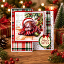 A handmade Christmas greeting card displayed on a wooden table, surrounded by holiday decorations including wrapped gifts, pinecones, evergreen branches, and warm string lights. The card features a central photo of a sleeping kitten wearing a Santa hat and blanket, with red and green plaid borders and a circular 'Jingle Bells' badge.