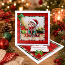 A square Christmas greeting card with a kitten in a Santa hat, displayed on a wooden surface with holiday decorations including ornaments, pine branches, and a candle in the background.
