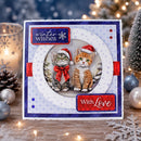 A handmade Christmas greeting card featuring two illustrated kittens wearing Santa hats, displayed on a wooden surface with festive holiday decorations in the background.