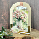A handmade arch-shaped greeting card featuring a watercolor illustration of pink roses in a floral vase, with the words 'In Our Prayers' at the top and 'Here for You' on an oval insert, displayed on a rustic wood slice with green leaves in the foreground.