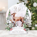 A festive Christmas tabletop decoration featuring a brown deer with antlers walking among snowy trees and holly, with a white banner at the bottom reading 'SENDING SPECIAL CHRISTMAS WISHES'. The decoration is displayed on a light surface with a blurred Christmas tree in the background.