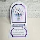 A handmade pop-up condolence card featuring white lilies in a vase, displayed open against a white brick wall background. The card includes a smaller pop-up tab reading 'Roght Sympathy' and a main message of condolence on a white card base with purple borders.