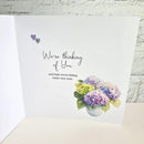 A white greeting card shown open against a white brick wall background. The card features the text 'We're thinking of You and hope you're feeling better very soon.