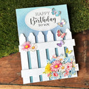 Birthday card with flowers, butterflies, and a white picket fence design on a wooden surface.