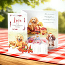 Two greeting cards with dog-themed designs on a picnic blanket outdoors.