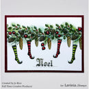 A square greeting card or art print featuring a festive Christmas design with green holly, red berries, pinecones, and hanging stockings in green, red, and black, with the word "Noel" at the bottom. The card is shown on a light gray background with small printed credits at the bottom.