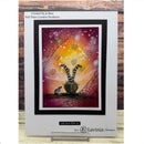 A handmade greeting card featuring a whimsical Halloween design with a cat inside a cauldron, spiderwebs, and a glowing orange and purple sky. The card is displayed on a small clear stand against a rustic wood plank background.