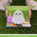 A handmade pop-up Halloween greeting card displayed on artificial grass. The card features a cute white cartoon ghost, a purple potion bottle, a jack-o'-lantern, books, and a spiderweb on a green background.