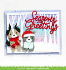 A handmade layered greeting card featuring two cute dog characters dressed in winter clothing, with a red 'Seasons Greetings' script overlay and a pastel winter forest background.