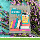 A handmade greeting card featuring a whimsical 'Have a Magical Day!' design, styled flat-lay on a textured turquoise fabric surrounded by purple flowers. The card features a gray wood-grain background with layered 3D elements including colorful books, a blue potion bottle, and gold stars.