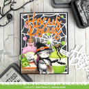 A Halloween-themed handmade card featuring a cartoon cat in a witch hat with a broom, surrounded by candy, spiderwebs, and the words 'Hocus Pocus' in orange. The card is displayed on a light wood background with crafting tools and die-cut decorations.