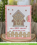 A handmade Christmas greeting card featuring a gingerbread house design, candy canes, and gingerbread men cutouts, displayed on a wooden slice with cacti in the background.