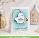 A handmade Halloween greeting card featuring a white ghost charm with a small pumpkin lantern, displayed on a white surface with decorative pumpkins and a house lantern in the background.