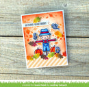A handmade autumn-themed greeting card featuring a cartoon scarecrow, pumpkins, birds, and falling leaves, with the text 'AUTUMN GREETINGS!' at the top, photographed on a rustic wooden surface.
