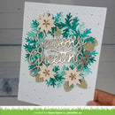 A handmade holiday greeting card held by a hand, featuring layered die-cut paper snowflakes and poinsettias in teal, gold, and cream, with a central metallic script reading 'Season's Greetings'.