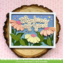 Card with 'thinking of you' text and flowers on a wooden slice against a pink background