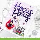 A handmade Halloween-themed card featuring the glittery purple text 'Hocus Pocus' on a pale lavender background, decorated with a red and purple witch hat, colorful potion bottles, a gray cat illustration, and a hanging tag reading 'HOCUS POCUS MAGIC COST $1'.