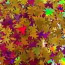Multicolor metallic autumn leaf confetti sprinkles in gold, purple, red, and green, overlapping to form a textured pattern.