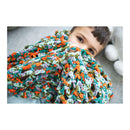 Child peeking out from under a colorful knitted blanket on a light gray surface.