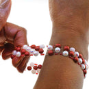 Close-up of a wrist wearing a red and white beaded bracelet against a pink background