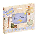 A boxed craft kit labeled 'Set Die Cuts' with a travel-themed design. The package shows illustrated postcards, directional signs, a backpack, boots, and a shell with a cross, on a light beige background.