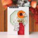A handmade greeting card by Penny Black, featuring a layered design with a red milk jug filled with orange and white flowers, set against a light green and white geometric background with the quote 'Gratitude is the art of seeing with your heart'.