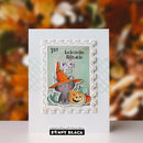 A handmade Halloween-themed greeting card featuring a gray cat in an orange witch hat next to a jack-o'-lantern, set against a scalloped white border with the text 'look on the bright side'. The card is displayed on a white surface with a blurred autumn-themed background, and the brand 'PENNY BLACK' is visible at the bottom.
