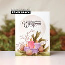 A handmade Christmas greeting card by Penny Black, featuring watercolor-style illustrations of purple and pink candles, pinecones, and evergreen branches on a white background. The card is displayed upright against a softly blurred holiday-themed backdrop.