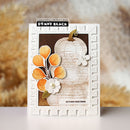 A handmade autumn-themed greeting card by Penny Black, featuring a white embossed border, a faux pumpkin design, orange and white paper flowers, and a brown background, displayed on a light surface with a blurred beige background.