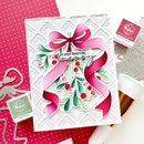 A handmade Christmas greeting card featuring a large pink ribbon bow, green holly leaves, red berries, and the phrase 'Let your heart be merry' in black script. The card is styled on a white surface with pink polka-dot paper, metal die-cut shapes, and Ranger ink pads visible around it.