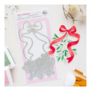 A flat-lay of a craft die-cut sheet featuring a silver metal holiday mistletoe die and a matching red, green, and pink paper cutout, displayed on a white background with crafting tools and embellishments.