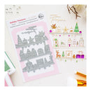 A flat-lay product photo of a 'Holiday Treasures' double-sided premium steel stamp set by Pinky Doodle Press. The set includes a silver steel stamp plate on a pink backing card, alongside a coordinating stamped paper sample sheet showing various holiday motifs like houses, stars, and trees in pastel colors.