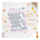 A flat-lay product photo of a 'Tiny Tidings' double-purpose steel press plate by Pinky Pretty. The silver metal plate is displayed on a pink backing card, surrounded by festive gold and white decorative stickers on a white background.