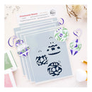 A flat-lay of layered acrylic stamping plates with floral and pumpkin stencil designs, shown alongside three finished layered sample ornaments with purple, green, and white floral patterns on a light pink background.