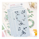 Four rectangular stamping plates with navy floral leaf stencils are arranged on a light surface, with stamped floral wreath and branch designs around them. A stamp card reading 'Seasonal Sprigs' and 'R.