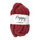 A skein of chunky, plush mohair-style yarn in a deep rust red color, wrapped with a white paper label that reads 'Poppy CRAFTS'.