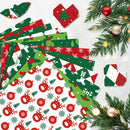 A flat-lay arrangement of colorful Christmas-themed paper cutouts and patterned sheets on a light background, surrounded by pine branches and ornaments.