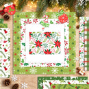 A flat-lay arrangement of Christmas-themed paper sheets and wrapping paper designs on a wooden surface, decorated with pine branches, lights, pinecones, and small wrapped gifts. The central sheet shows a festive holiday pattern with red poinsettias, green leaves, white snowflakes, and candy canes, surrounded by coordinating patterned papers.