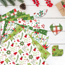A styled flat-lay of multiple sheets of Christmas-themed patterned paper on a white wood background, surrounded by holiday props like pine branches, a pinecone, red berries, and a small kraft gift box.