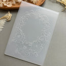 A translucent white silicone mold with an embossed floral wreath design, displayed diagonally on a gray surface with dried flowers in the background.