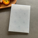 A translucent rectangular silicone mold with a raised geometric diamond pattern, shown on a gray surface with a wooden tray and dried flowers in the background.