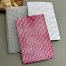 Three textured rectangular cards or envelopes with a knit-like vertical pattern, shown overlapping on a neutral gray surface. The front card is pink with a gradient from light to deep pink, the back card is white, and the third card is translucent gray.