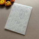 A translucent white silicone mold with embossed winter holiday designs, including pine trees, pinecones, hearts, and a bow, shown on a neutral gray background with dried flowers in the corner.