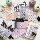 A styled flat-lay of multiple sheets of coordinating paper with Halloween-themed patterns including ghosts, pumpkins, stars, stripes, and checkers in pastel colors. A black label in the center reads 'spooky coordinating paper,' and a sample card showing a ghost illustration is placed on the lower right.