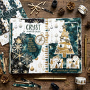 An open handmade journal spread displayed on a rustic wooden surface, surrounded by decorative craft props including pinecones, gold pens, washi tape, pencils, and matching journaling paper. The journal pages feature a winter galaxy theme with teal and white watercolor textures, gold foil stars and trees, snowflake cutouts, and decorative text reading 'CRYST' and 'MY WONDERLAND JOURNAL'.