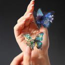 Two decorative butterfly-shaped rings with floral details are shown on a person's fingers against a dark gray background.