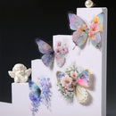 Four pastel butterfly and floral wall decals arranged on white stepped display blocks against a black background. A small white cherub figurine sits on the left block.