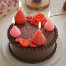 Chocolate cake with strawberry candles and 'Happy Birthday' text on a white surface.