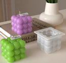 A set of grape-shaped candles and a matching silicone mold on a tabletop. The set includes two grape cluster candles, one purple and one green, each with a small 'Welcome' tag, alongside a translucent white silicone mold.