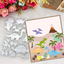 A dinosaur-themed craft kit shown on a light surface with decorative flowers and a radio prop. The set includes a printed card or sheet with colorful dinosaurs, palm trees, an volcano, and footprints, alongside a clear metal cutting template with matching dinosaur shapes.